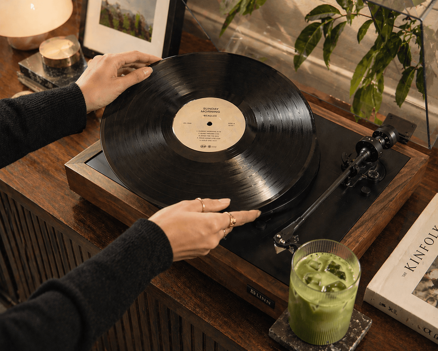 Hands placing a record on a turntable beside a matcha drink